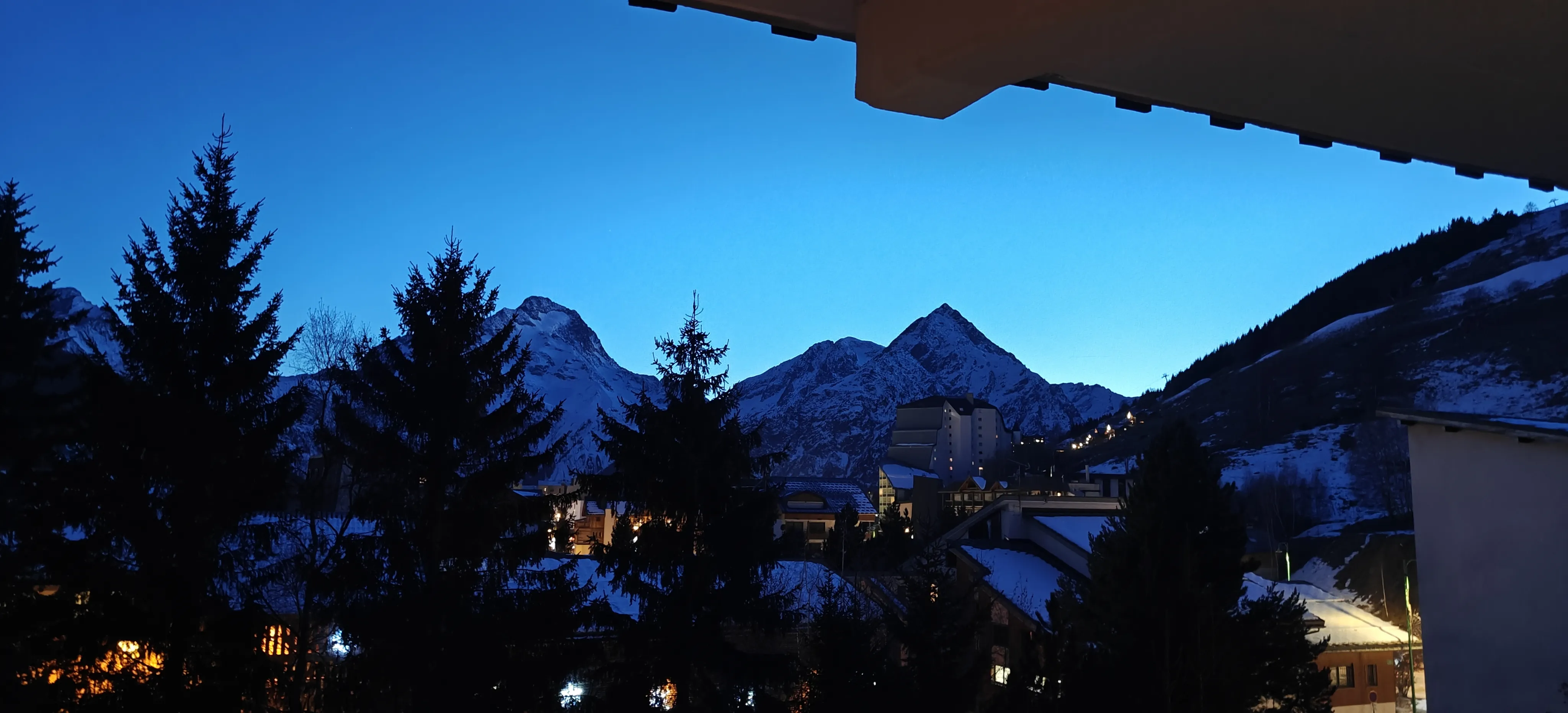 Snowy alpine village and mountain peaks at blue hour under a bright evening sky
