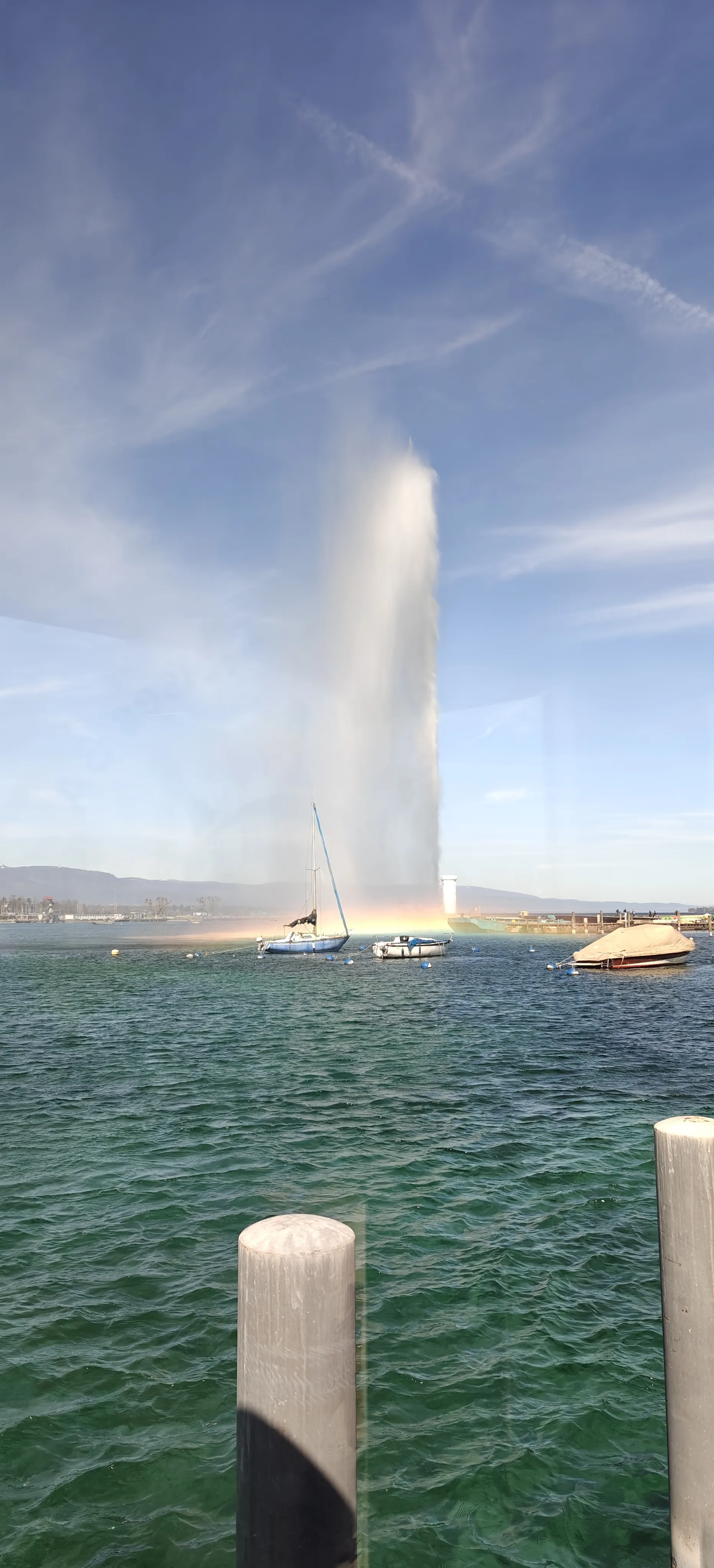 A tall column of water rising from a lake with boats nearby under a blue sky