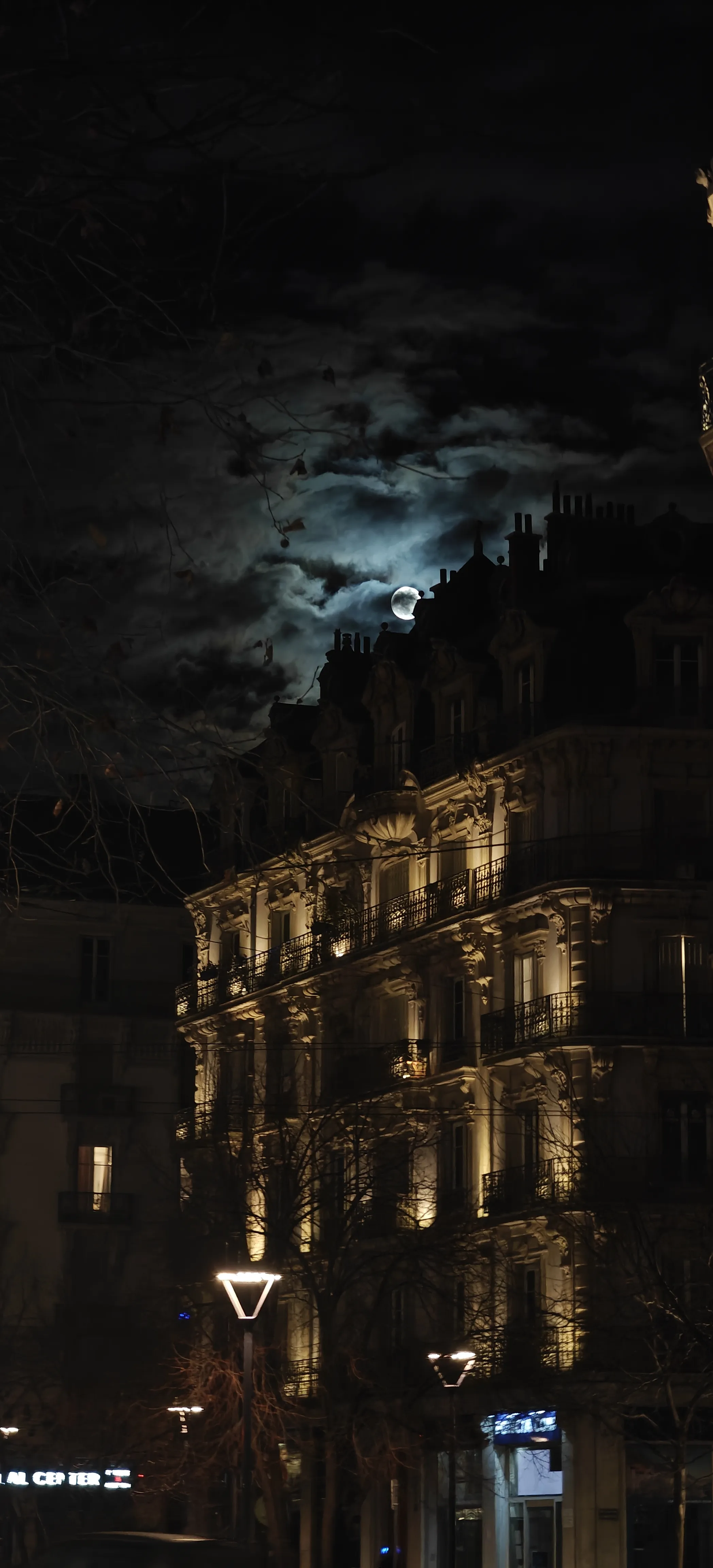 A lit historic building under a cloudy night sky with the moon behind it